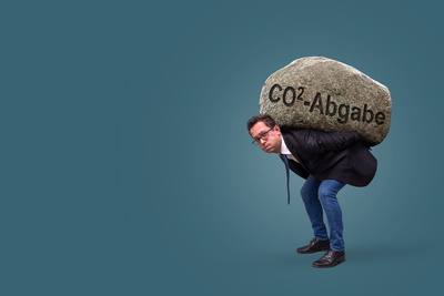 Mann trägt Stein mit Aufschrift CO2 Abgabe